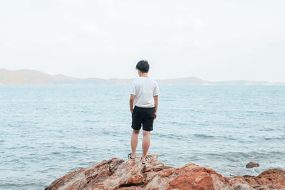 Rear view of man standing on rock by sea against sky