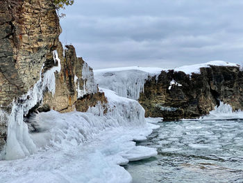 Scenic view of ice covered shore against cliff and sky