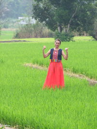 Portrait of smiling woman gesturing thumbs up while standing on grassy field