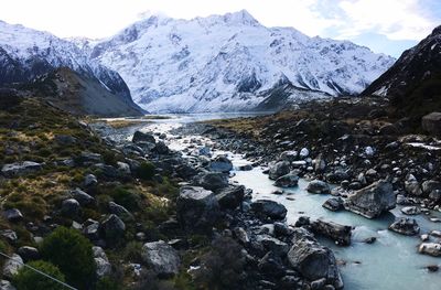 Stream by snowcapped mountains against sky