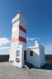 Lighthouse by sea against clear blue sky