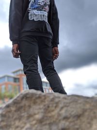 Midsection of man standing on rock against cloudy sky