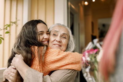 Cheerful girl and senior woman embracing at entrance of house