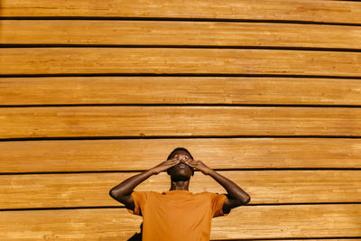 Man with hands covering eyes in front of orange wall at sunset