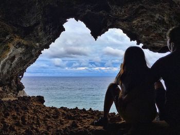 Rear view of father and daughter sitting at cave against sea