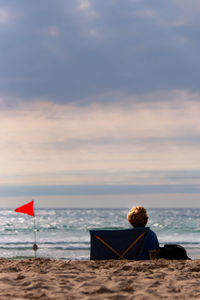 Woman sitting on beach against sky during sunset