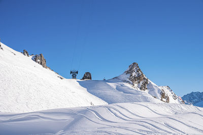 View of ski tracks on snowy mountain against clear blue sky