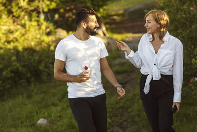 Smiling man and woman talking while walking on grassy field