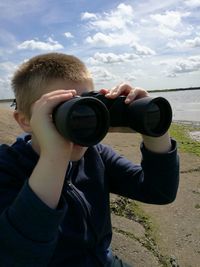 Boy looking through binocular against cloudy sky