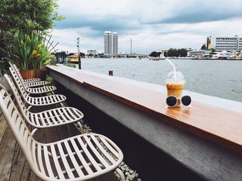 Empty seats by coffee and sunglasses on retaining wall against chao phraya river