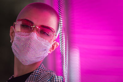 Portrait of young woman with shaved head wearing mask standing against abstract backgrounds