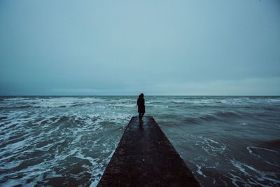 Rear view of man walking on beach against clear sky
