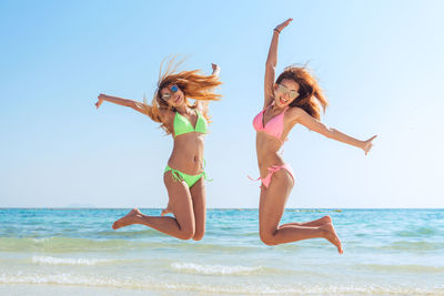 Female friends in swimwear jumping at beach against clear sky