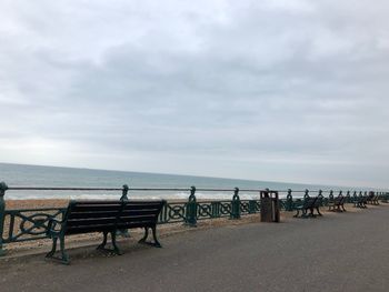 Empty benches on beach against sky