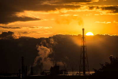 Silhouette factory against sky during sunset