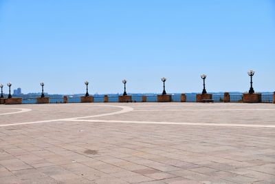 Empty footpath by street against clear blue sky