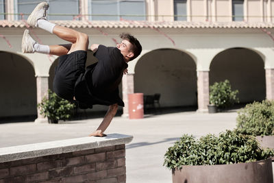 Side view of concentrated male jumping over stone fence and balancing on arm while performing stunt and doing parkour