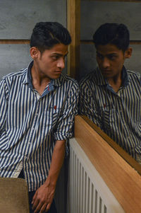 Young man looking away while standing against wall