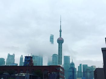 Low angle view of communications tower in city against cloudy sky