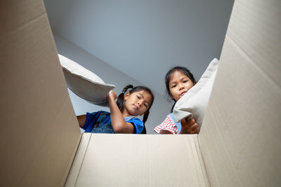 Low angle portrait of sibling putting pillow in cardboard box