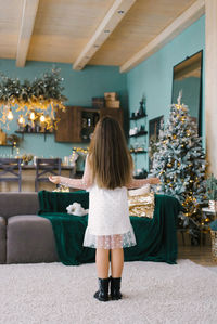 A girl with long hair stands with her back to the living room decorated for christmas