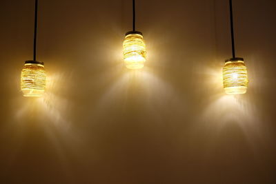 Illuminated jars hanging against wall at night
