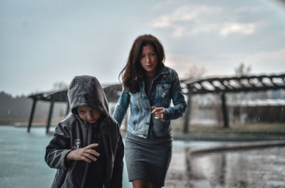 Portrait of friends standing on bridge over river against sky