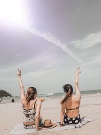 Rear view of female friends showing peace signs at beach