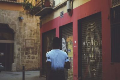 Rear view of man walking on alley amidst buildings in city