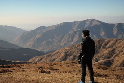 Rear view of man standing on field against mountains