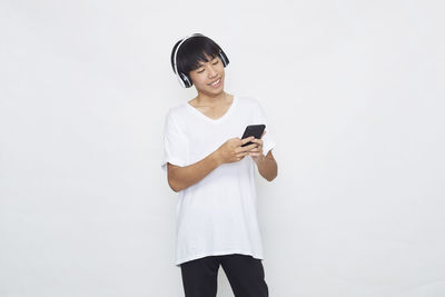 Young woman using phone while standing against white background