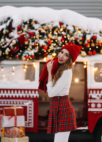 A beautiful young woman with red lips in a warm hat stands by a decorated christmas van on street