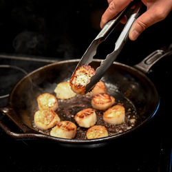 Close-up of human hand preparing food in cooking pan