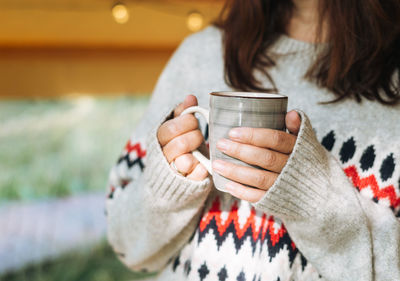 Brunette woman in nordic sweater drinking tea and relaxing in glamping in nature