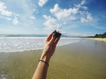 Close-up of hand on sea against sky