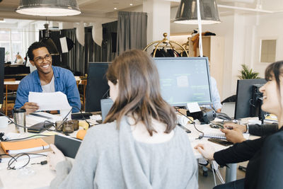 Cheerful male and female it professionals talking while sitting at desk in creative office