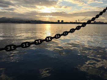 Close-up of silhouette chain over river against cloudy sky during sunset