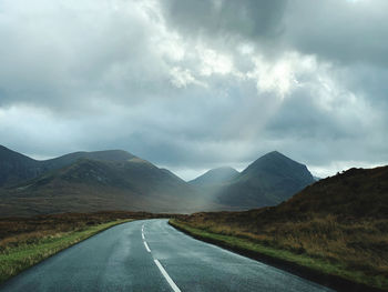 Empty road along landscape against cloudy sky