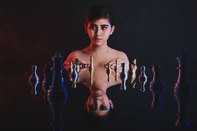 Portrait of young woman with chess pieces reflecting against black background