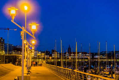 Illuminated street against blue sky at night