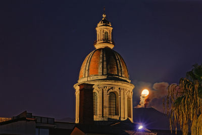 The basilica of riposto illuminated against the  sky and the moon setting among the fumes of etna