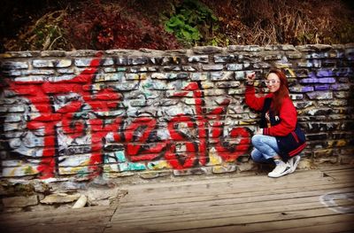 Woman standing by graffiti on brick wall