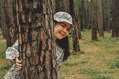 Portrait of smiling young woman by tree trunk in forest