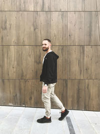 Full length of young man standing on footpath against wall