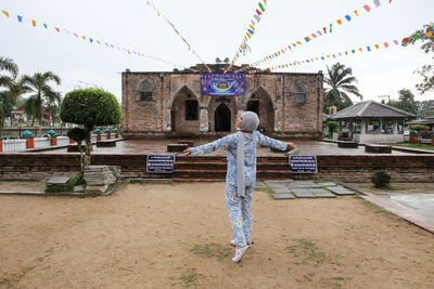 Rear view of man standing outside temple against building