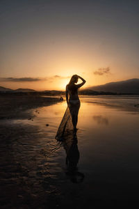 Woman walking at beach against sky during sunset