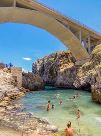 People swimming in sea against bridge