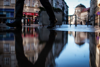 Surface level of man walking by puddle on footpath in city