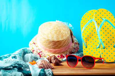 Close-up of sunglasses with hat and towel on table against blue background
