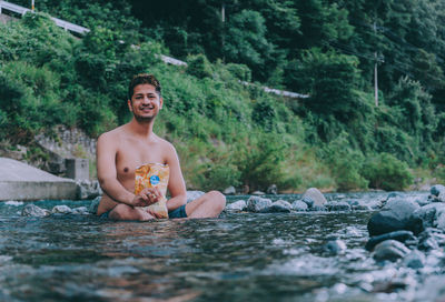 Full length of shirtless man sitting in forest
